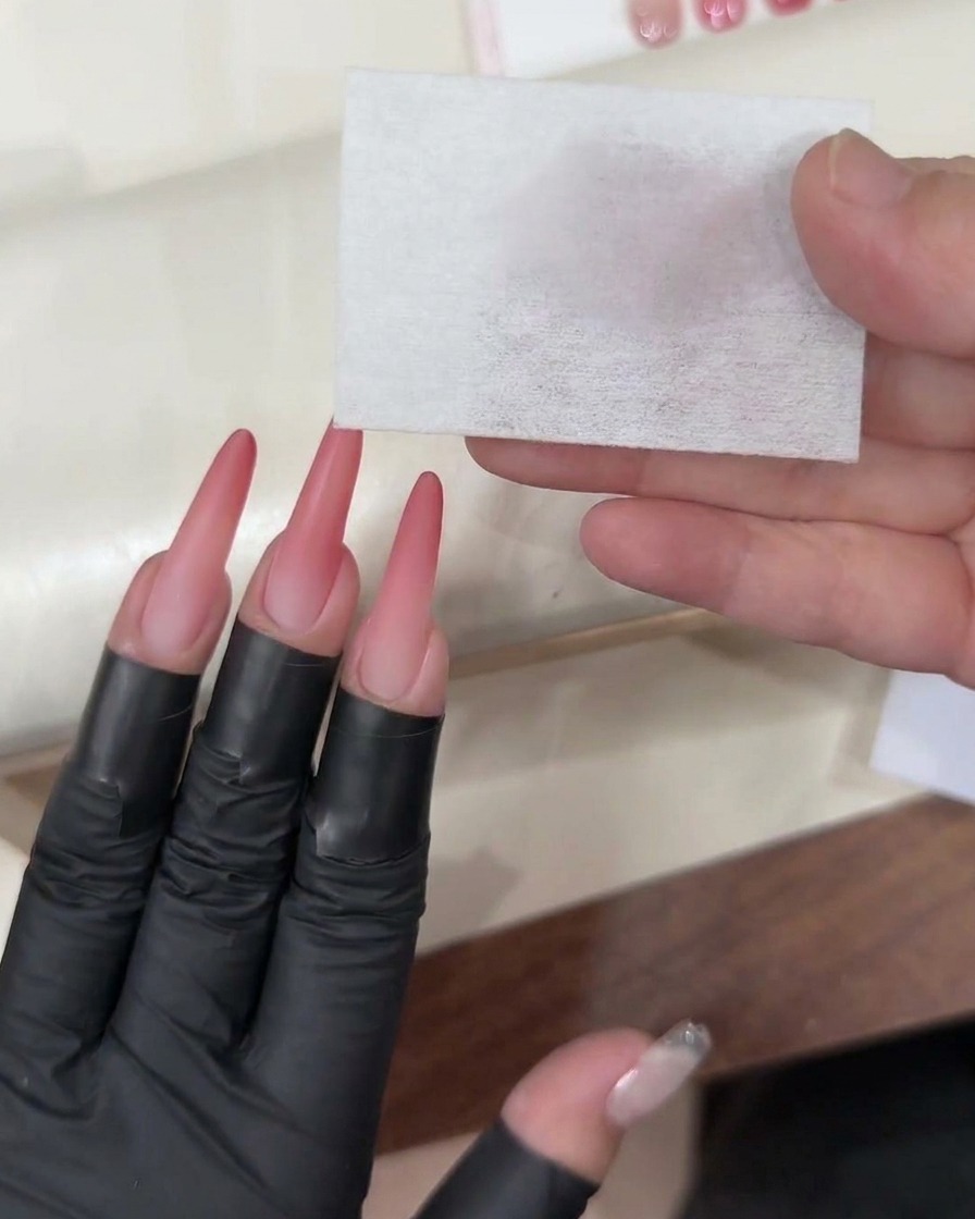 Un pennello da gel che applica un top coat trasparente e lucido sullunghia ombré rosa completata.