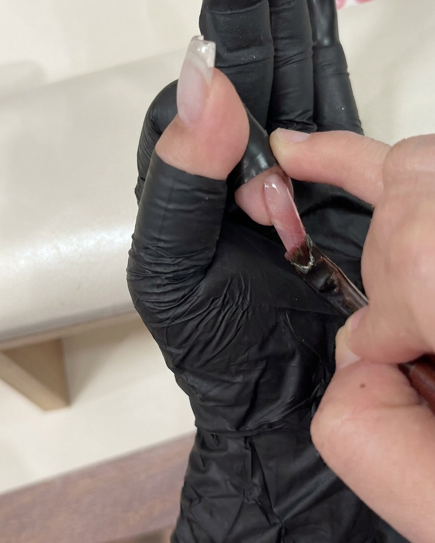 Un paio di pinzette che posizionano con cura un piccolo charm decorativo su ununghia con top coat ancora umido.