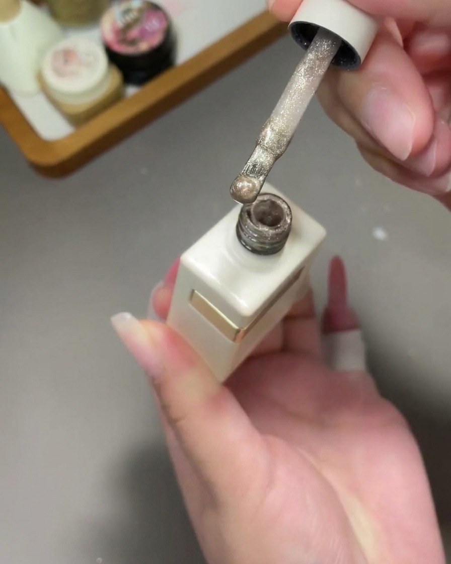 Pennello che applica uno smalto gel cat-eye oro glitterato sopra lunghia sfumata.