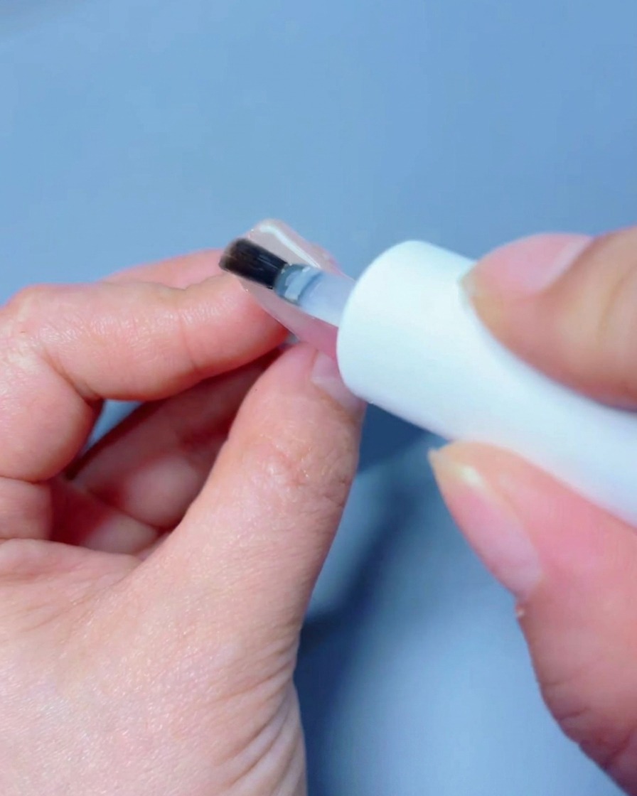 Una mano posizionata sotto una lampada professionale UV/LED per polimerizzare il top coat.