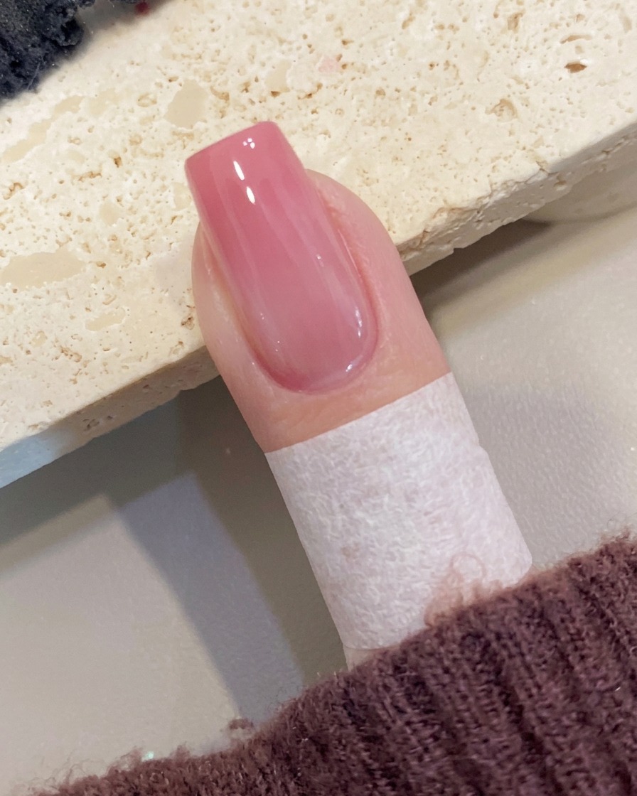 Un pennello applica uno strato finale di top coat lucido su ununghia ombré pesca.