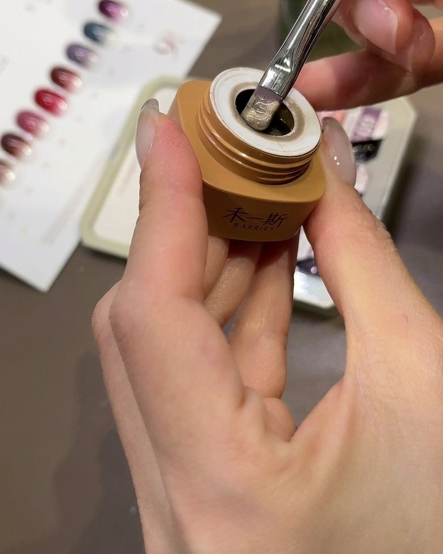 Un pennello applica gel cat-eye color pesca beige su una tip trasparente.