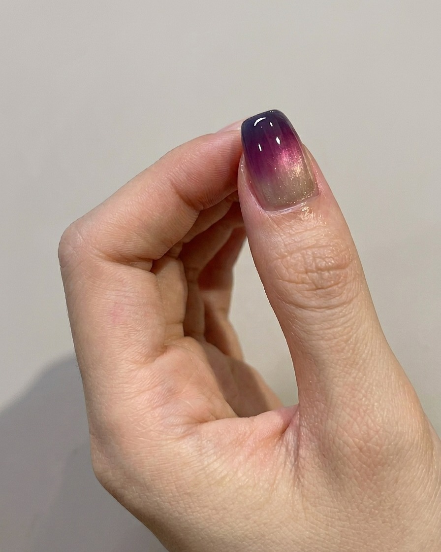 Un pennello applica un top coat lucido finale su ununghia sfumata blu-viola completata.