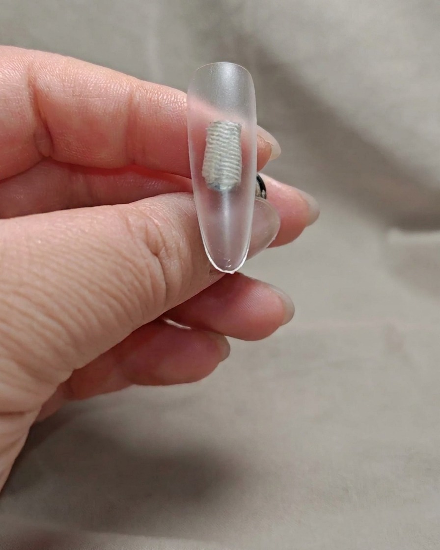 Un pennello applica un sottile strato di gel rosa nude trasparente sulla punta dellunghia.