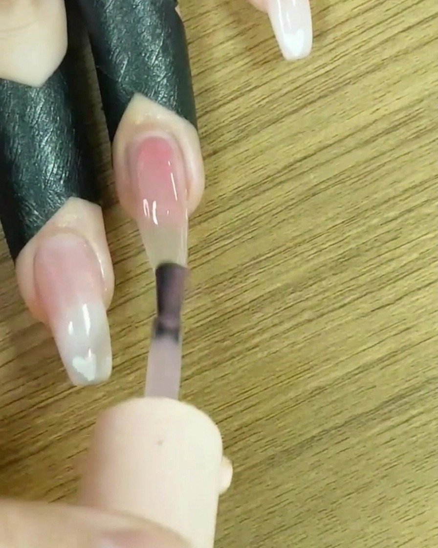 Un pennello che applica smalto gel nude trasparente sullintera superficie dellunghia.