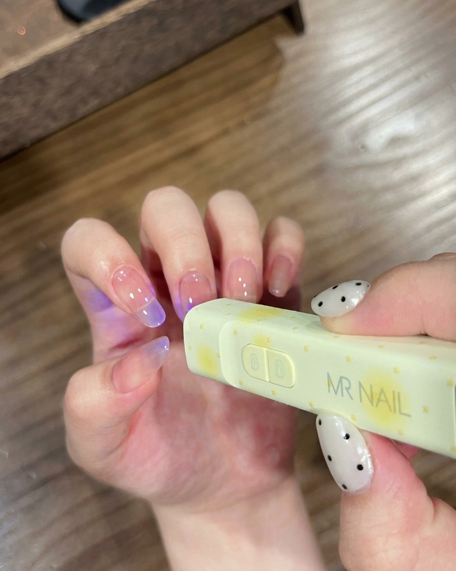 Unghie posizionate sotto una piccola lampada UV portatile a marchio MR NAIL per la polimerizzazione.