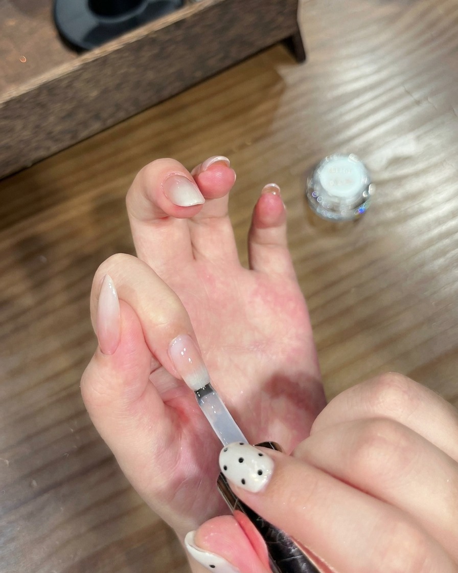 Un pennello che applica un top coat trasparente su ununghia finita con effetto sfumato e cromato.