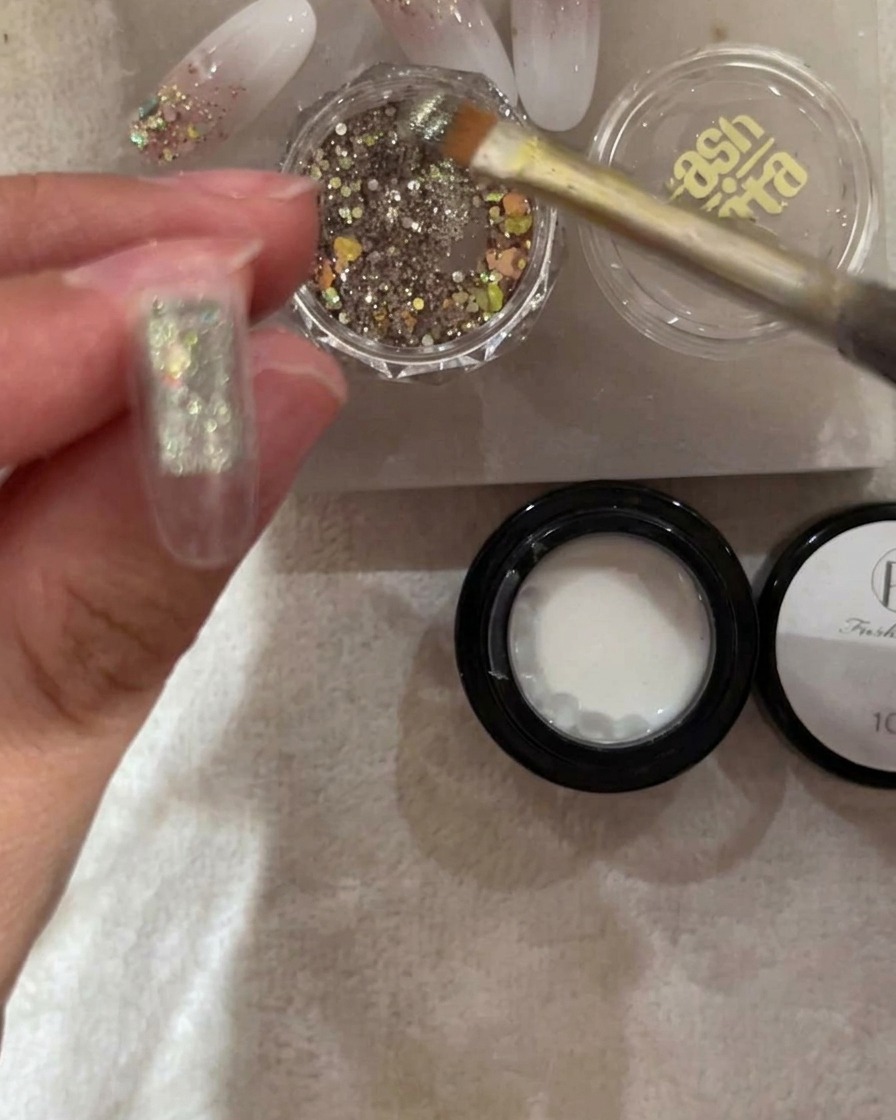 Un pennello applica glitter argento e cangianti sulla metà superiore di una tip trasparente.