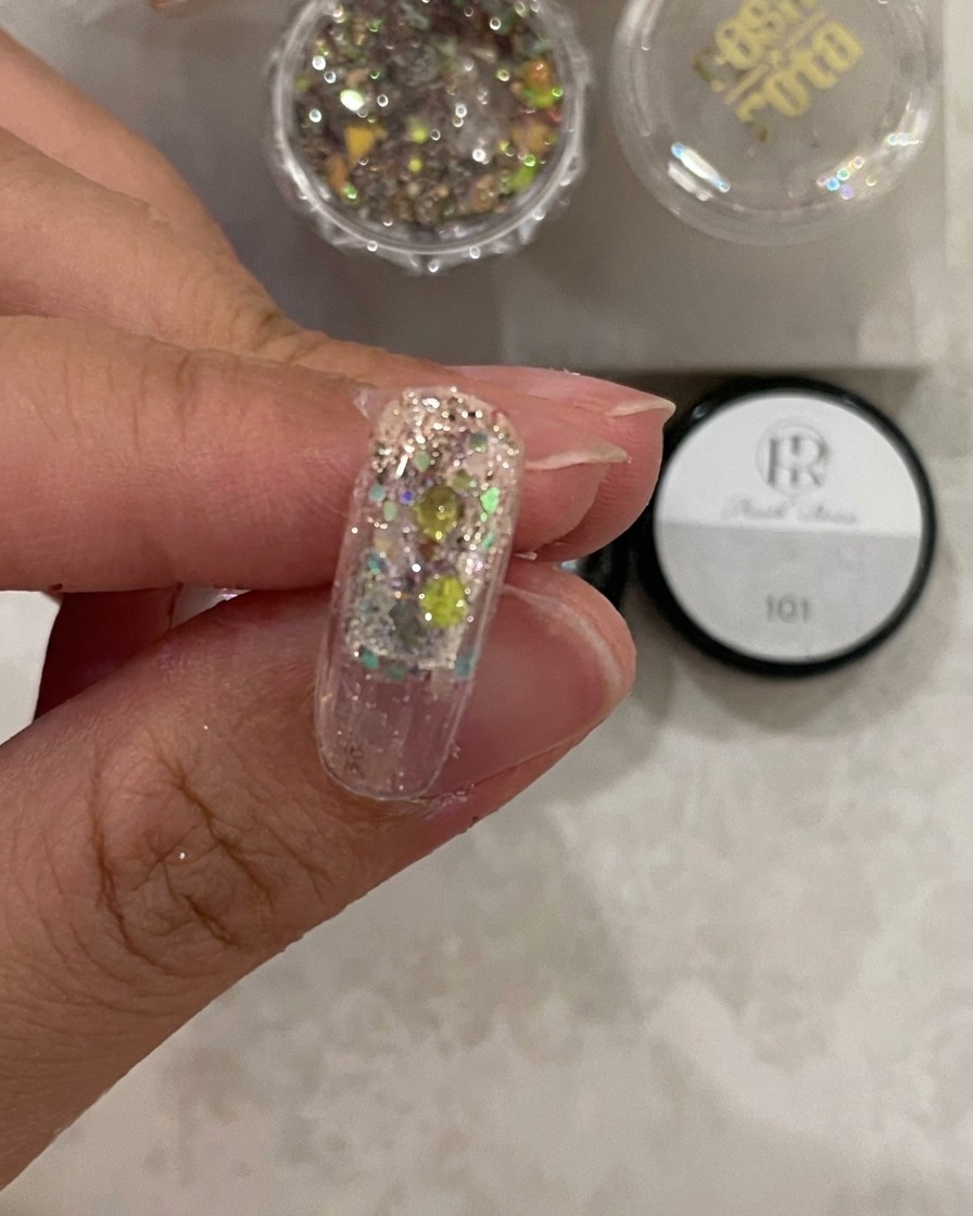 Primo piano di una tip sotto la luce della lampada, che mostra il gel costruttore fissato sopra i glitter.