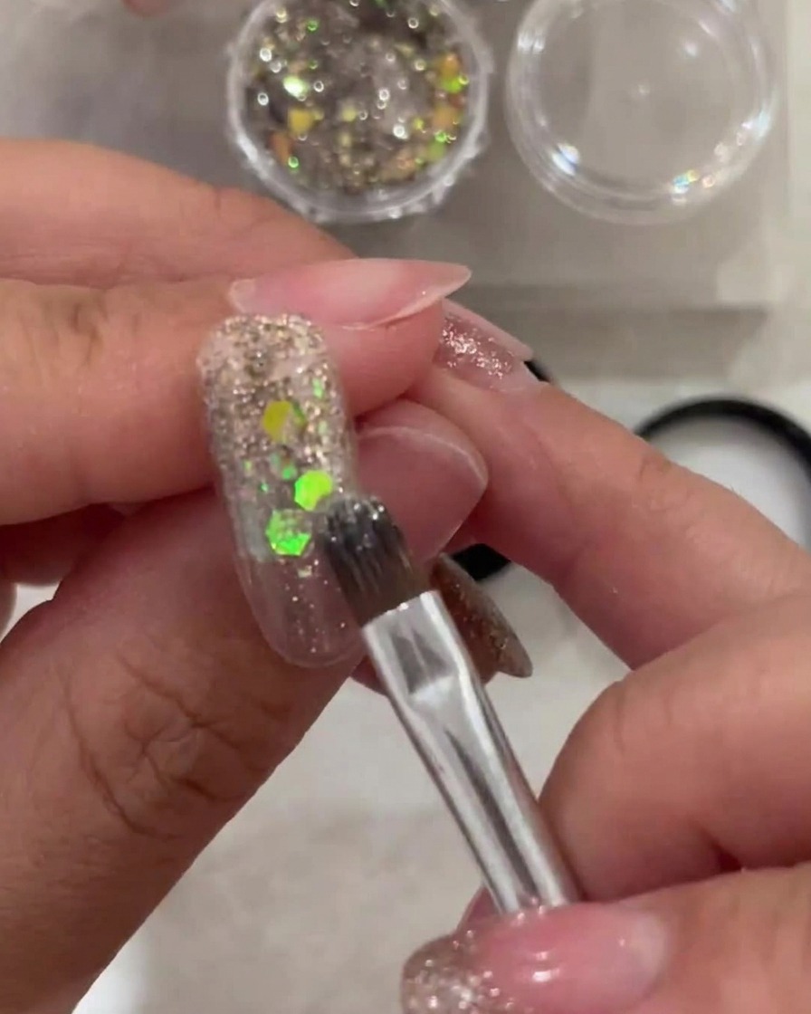 Un pennello applica uno strato sottile di gel bianco semi-trasparente sulla punta dellunghia, sfumando verso la zona glitterata.