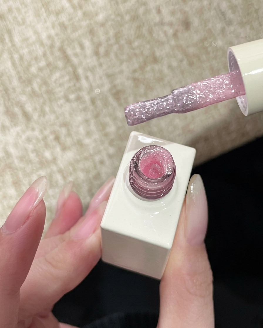 Un pennello da smalto che preleva un gel glitter rosa velato e scintillante, pronto per lapplicazione.