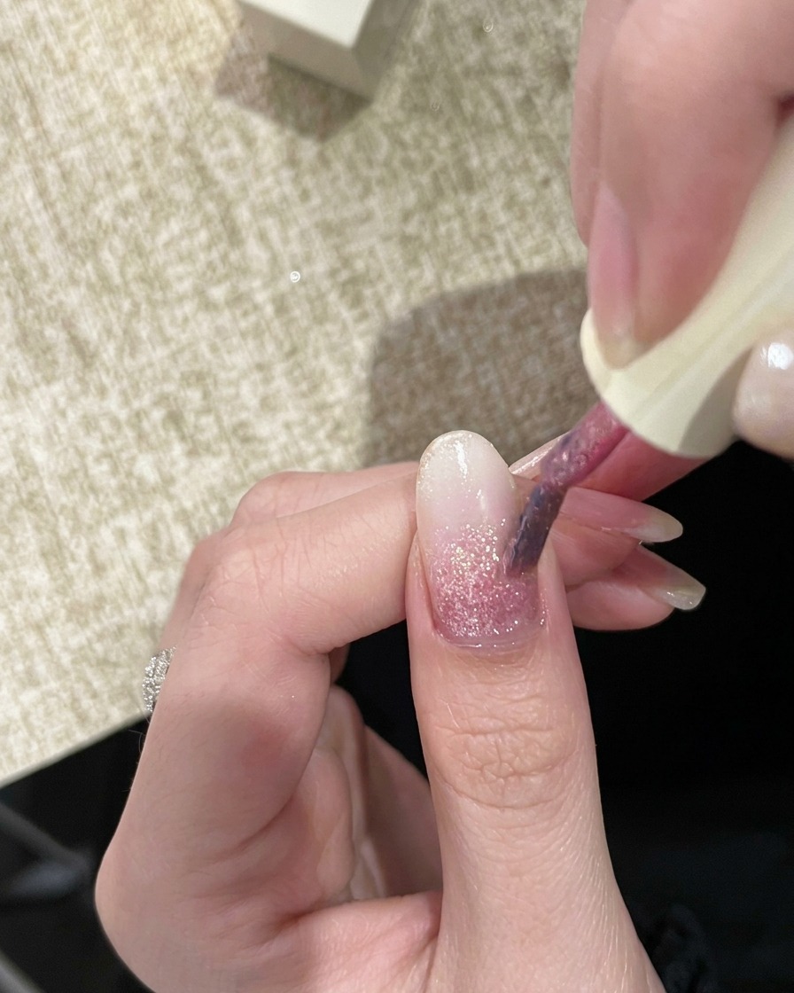 Un pennello da unghie che applica un secondo strato di gel glitter rosa leggermente più pigmentato.