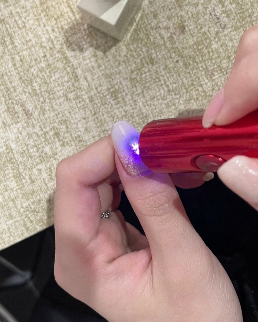 Una mano posizionata sotto una lampada UV portatile compatta, con la superficie dellunghia che risplende sotto la luce.