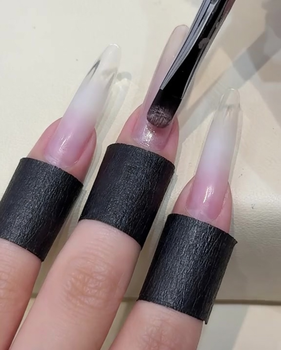 Un pennello che applica uno strato di gel polish cat-eye color nude sullunghia.