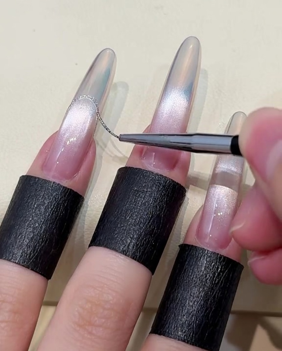 Primo piano di un pennello sottile che applica una linea di gel argento platino per creare una french su ununghia sfumata aurora.