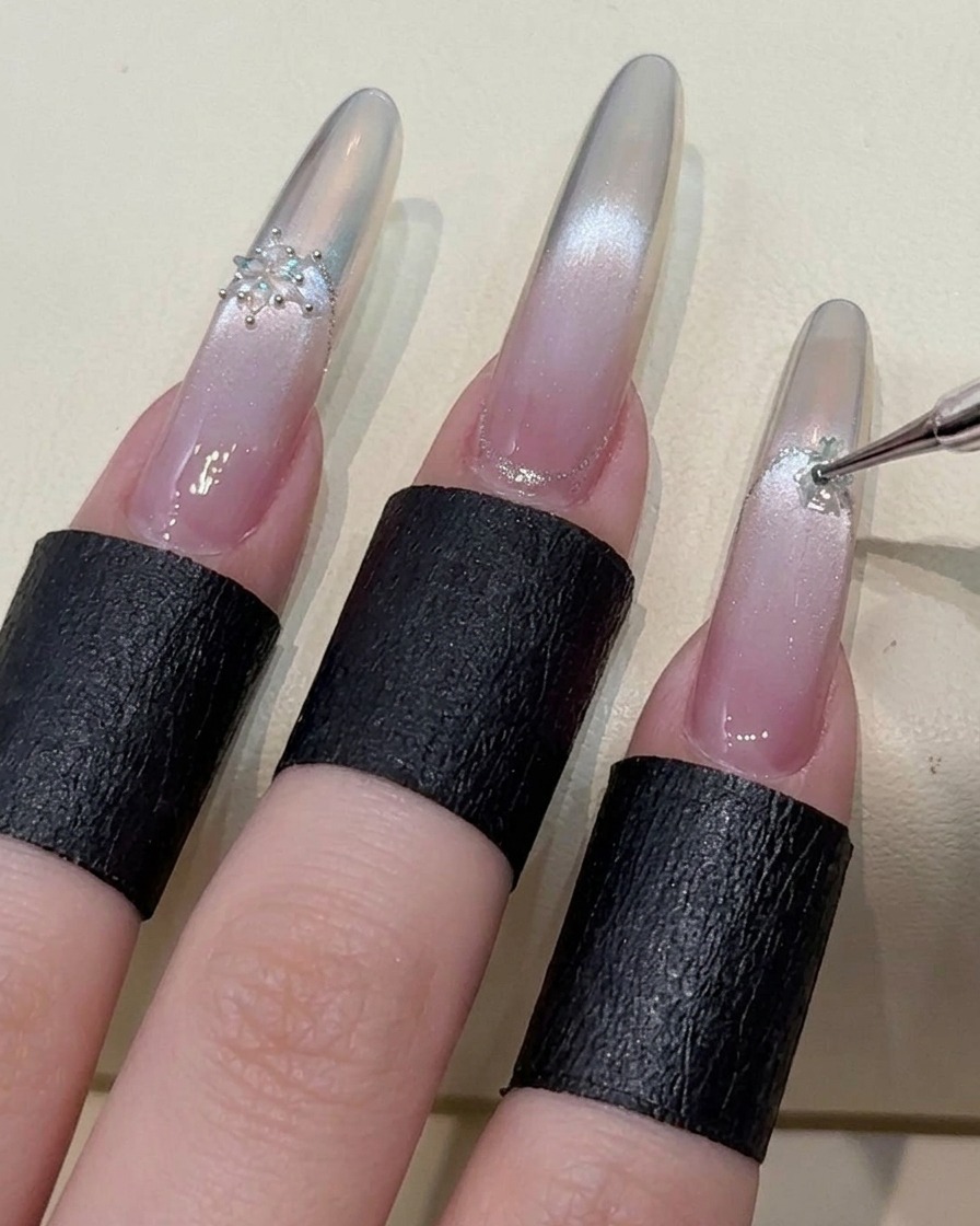 Un dito indice decorato con un accento di cristallo a fiocco di neve, evidenziando il processo dettagliato della nail art.