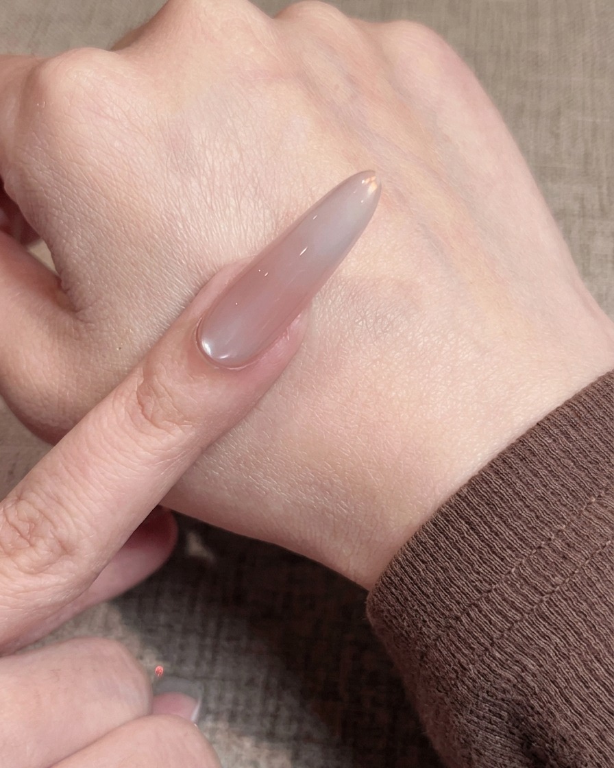 Primo piano di un pennello che applica un sottile strato uniforme di gel nude su ununghia preparata.