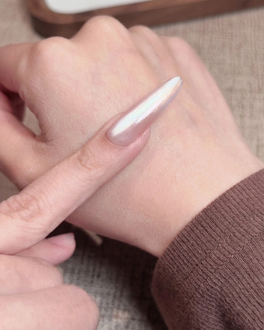 Un pennello applica un top coat rosa trasparente su ununghia con effetto blush, preparandola per la polimerizzazione finale.