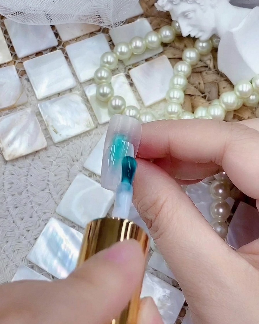 Un pennellino che applica uno strato di smalto gel bianco latte su una tip trasparente per unghie press-on.