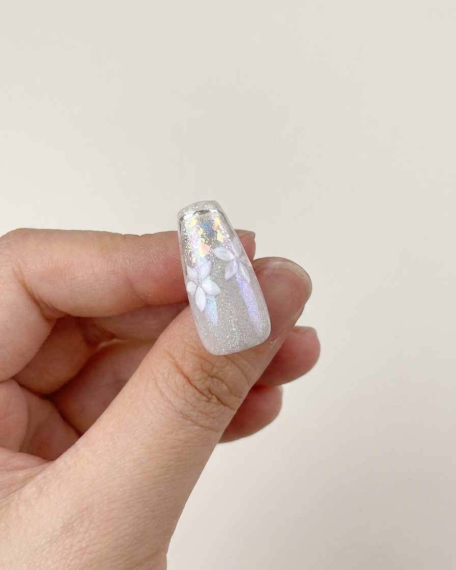 Un pennellino che applica uno strato di top coat lucido e trasparente sul design finito, con fiori bianchi e scaglie argentate.