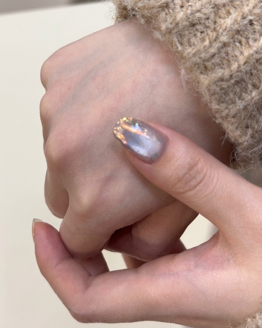 Un pennello che applica uno strato di smalto gel cat-eye argentato su ununghia naturale.