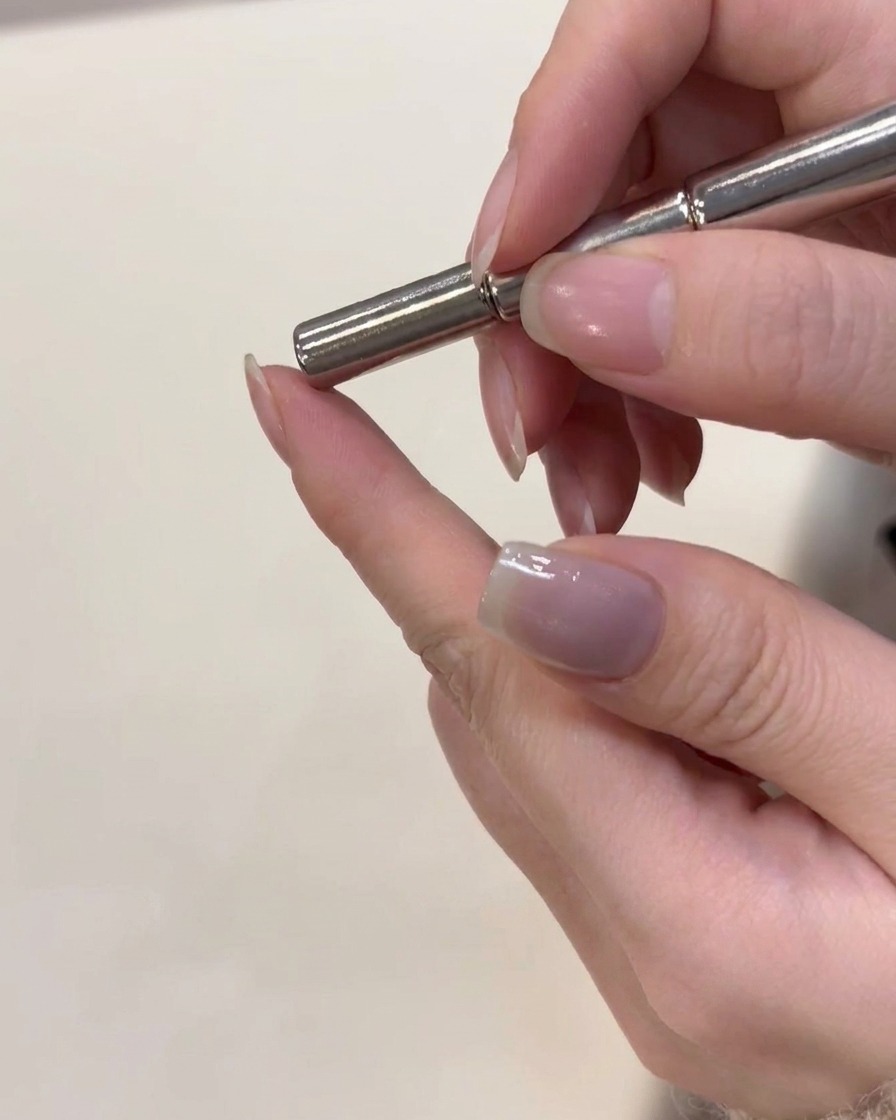 Un magnete tenuto appena sopra ununghia con gel cat-eye argentato fresco per modellare le particelle magnetiche.