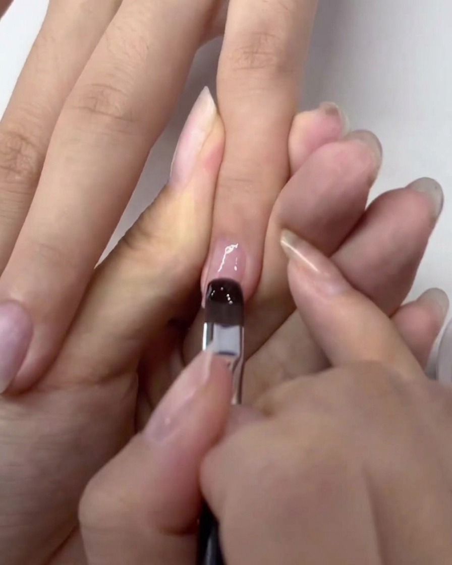 Un pennello applica uno strato trasparente di base gel su ununghia naturale preparata.