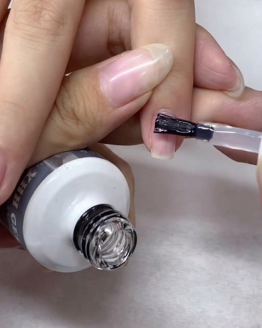 Un pennello da nail art stende e uniforma delicatamente il gel di rinforzo su tutta la superficie dellunghia.