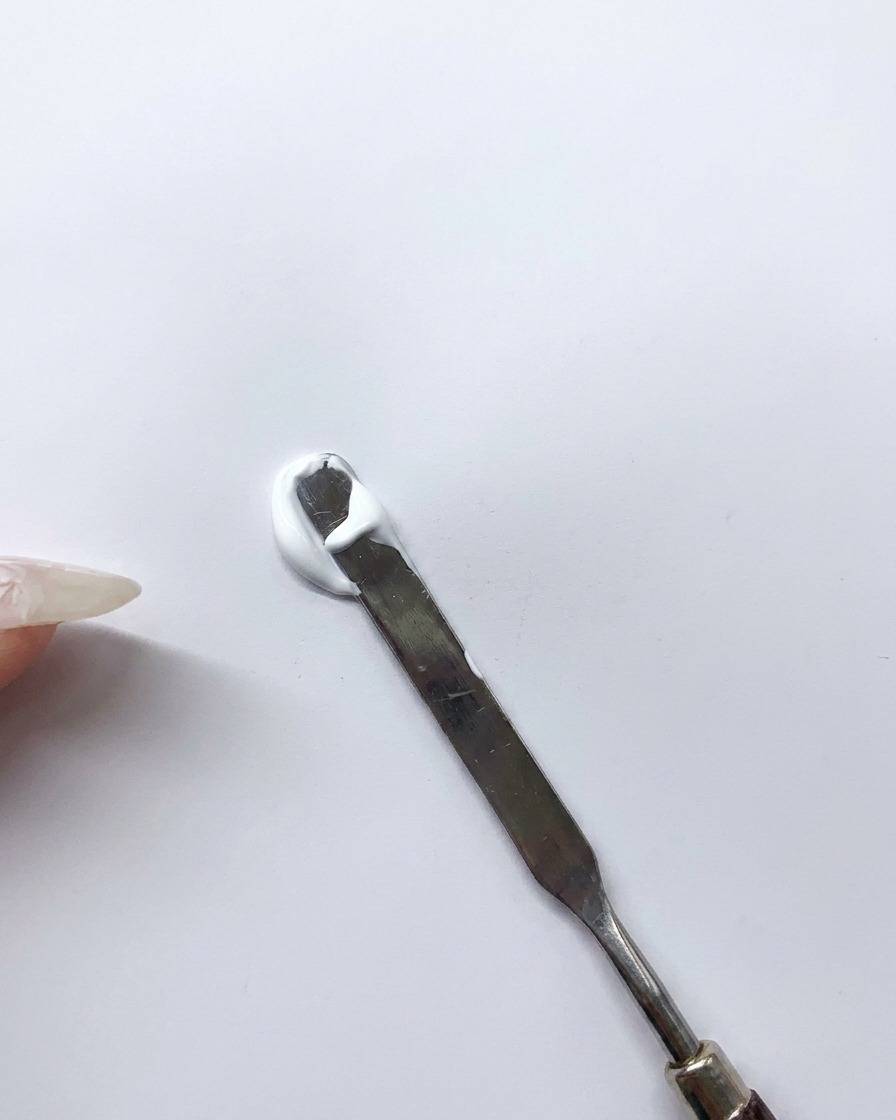 Una spatola metallica mescola una goccia di gel bianco e blu su una superficie pulita per creare una tonalità di azzurro.