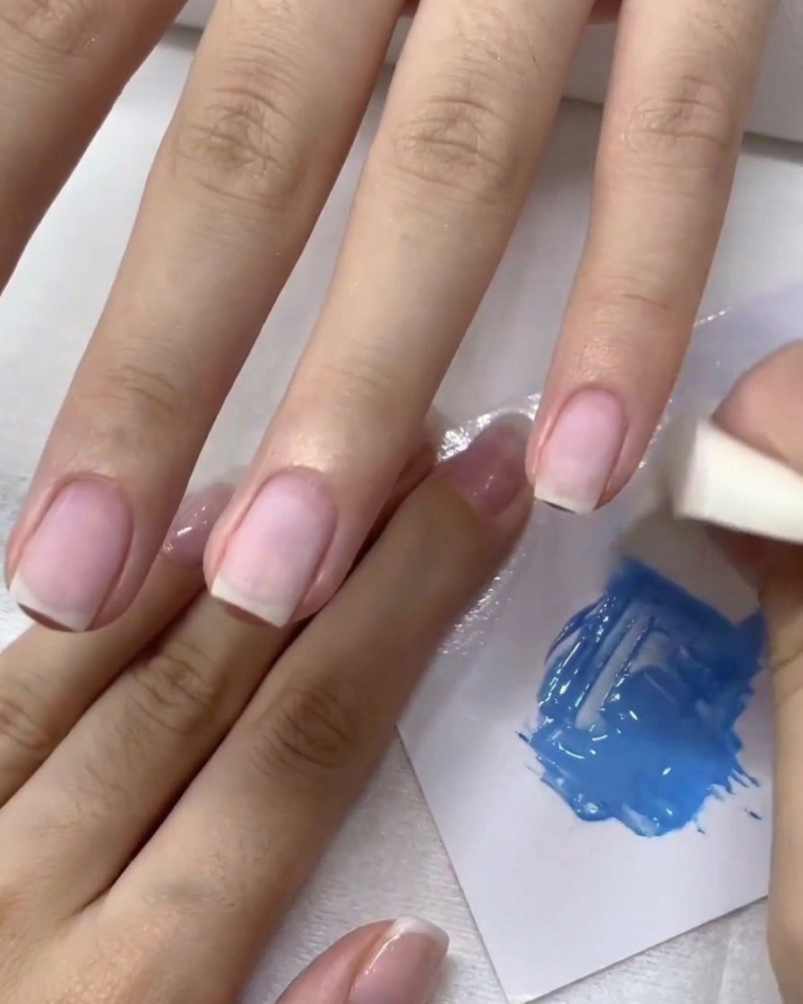Una spugnetta per il trucco tampona il gel blu sullunghia per creare un effetto ombré.