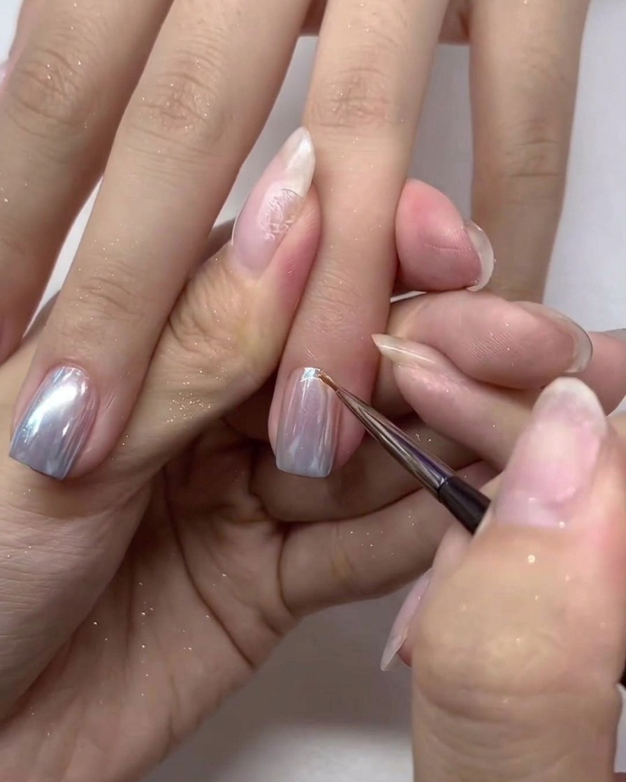 Un piccolo pennello per unghie applica con cura uno strato finale di top coat sulle unghie con effetto chrome.