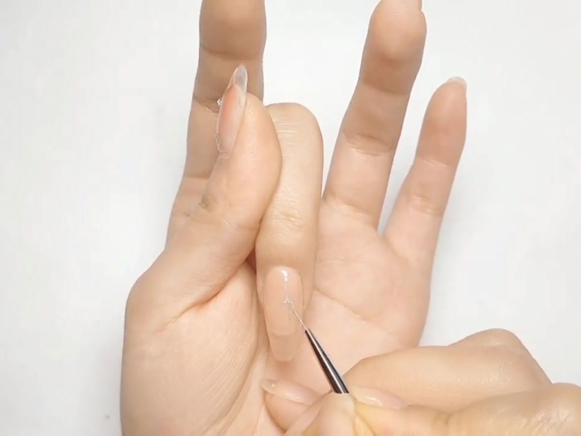 Un sottile pennello per nail art disegna una forma a croce argento su ununghia dipinta di nude.