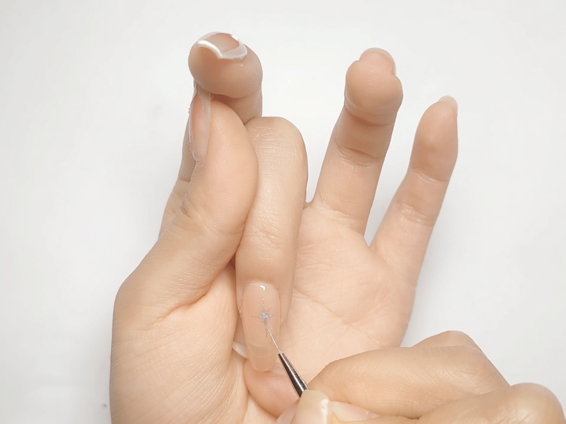 Un pennello per nail art riempie gli angoli a forma di diamante di una stella metallizzata argento su ununghia nude.