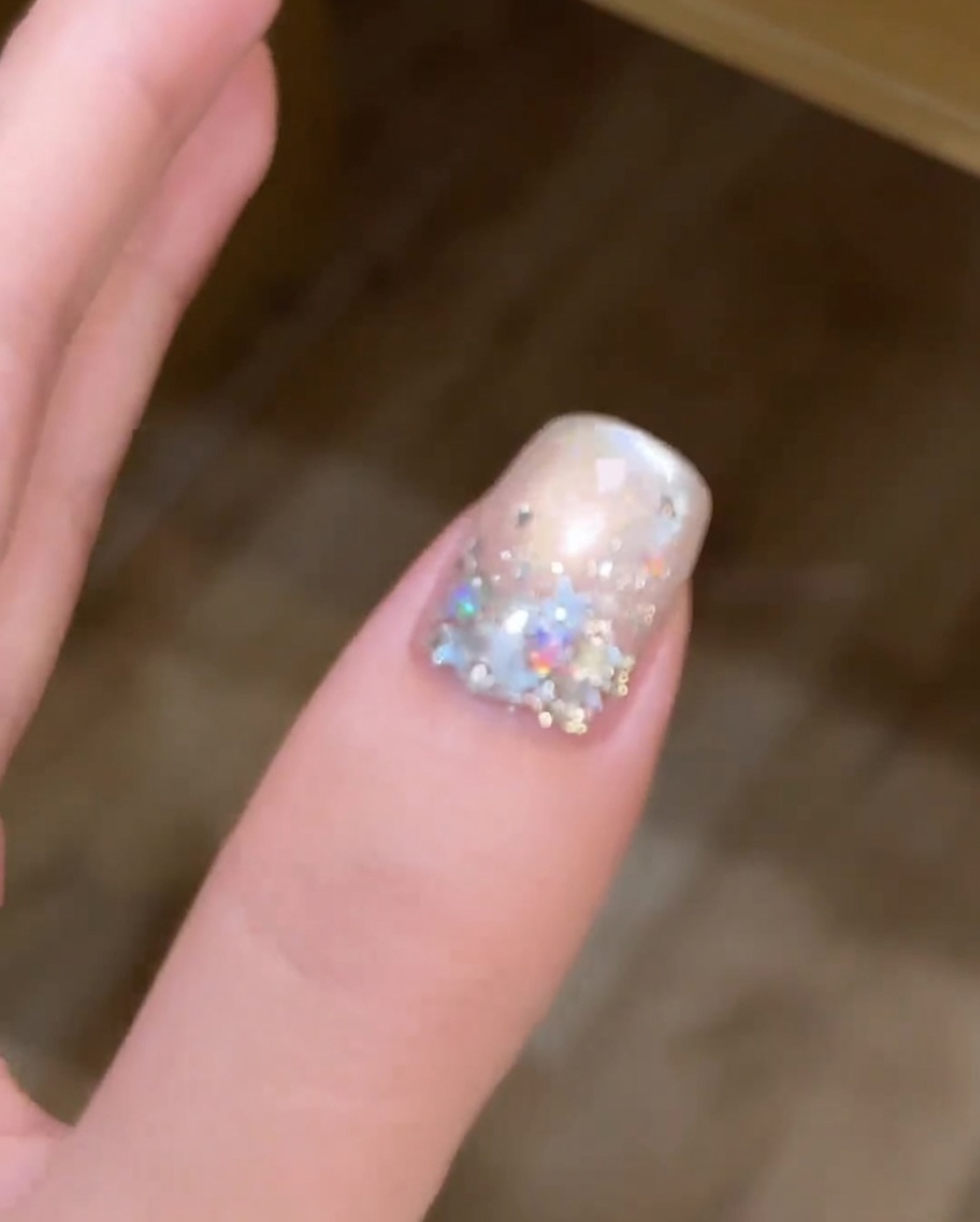 Un pennello che applica uno strato di smalto cat-eye metallizzato argento su ununghia dipinta di bianco.
