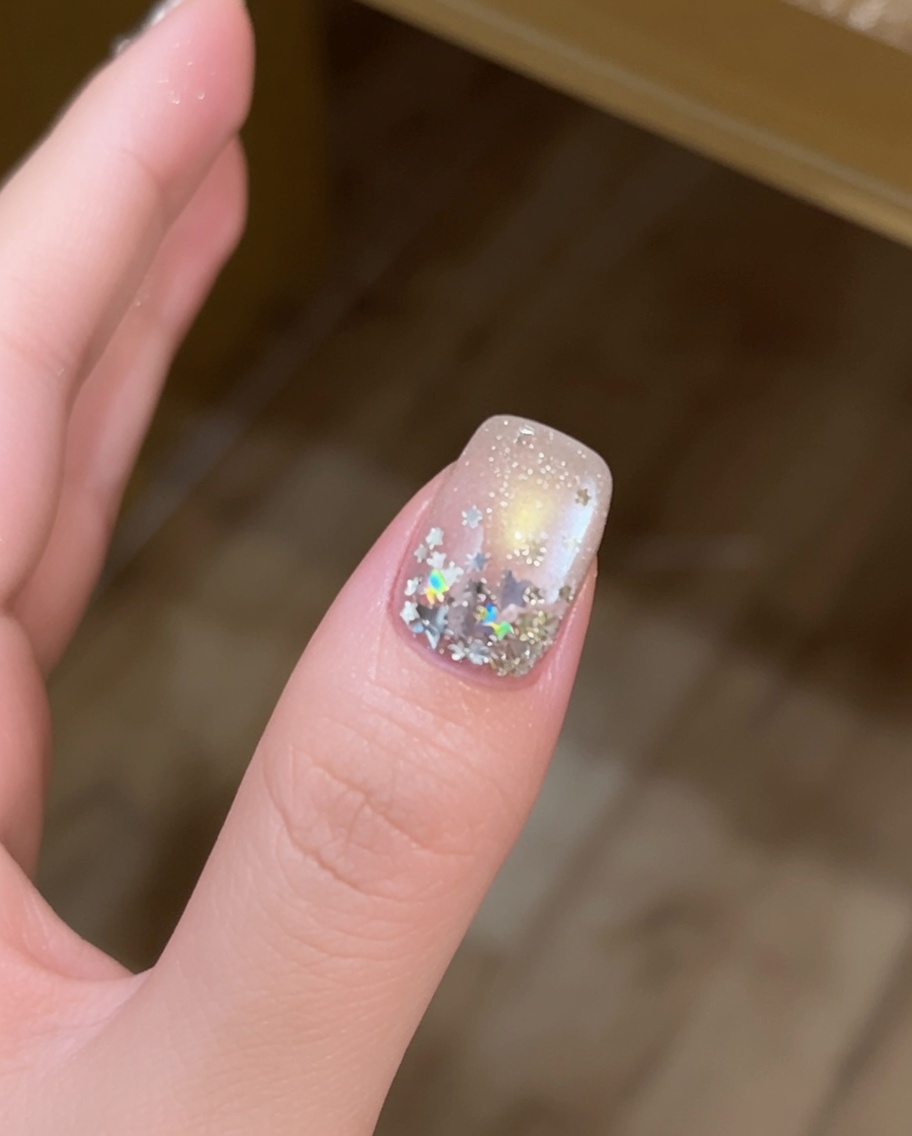 Primo piano di un dito con grandi stelle argentate posizionate su una superficie ungueale ricoperta di gel con un pennello a punta fine.