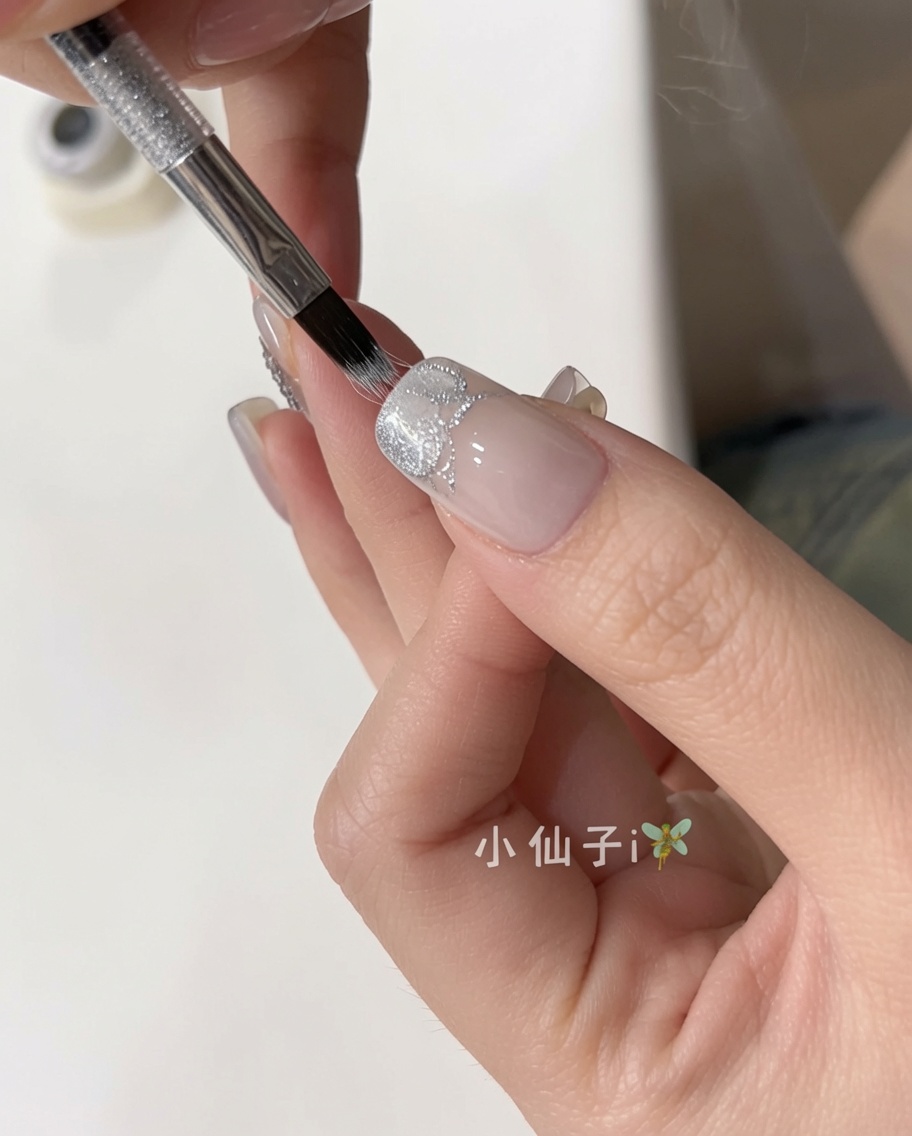 Un pennello applica uno smalto gel cat eye argento scintillante su ununghia naturale preparata.