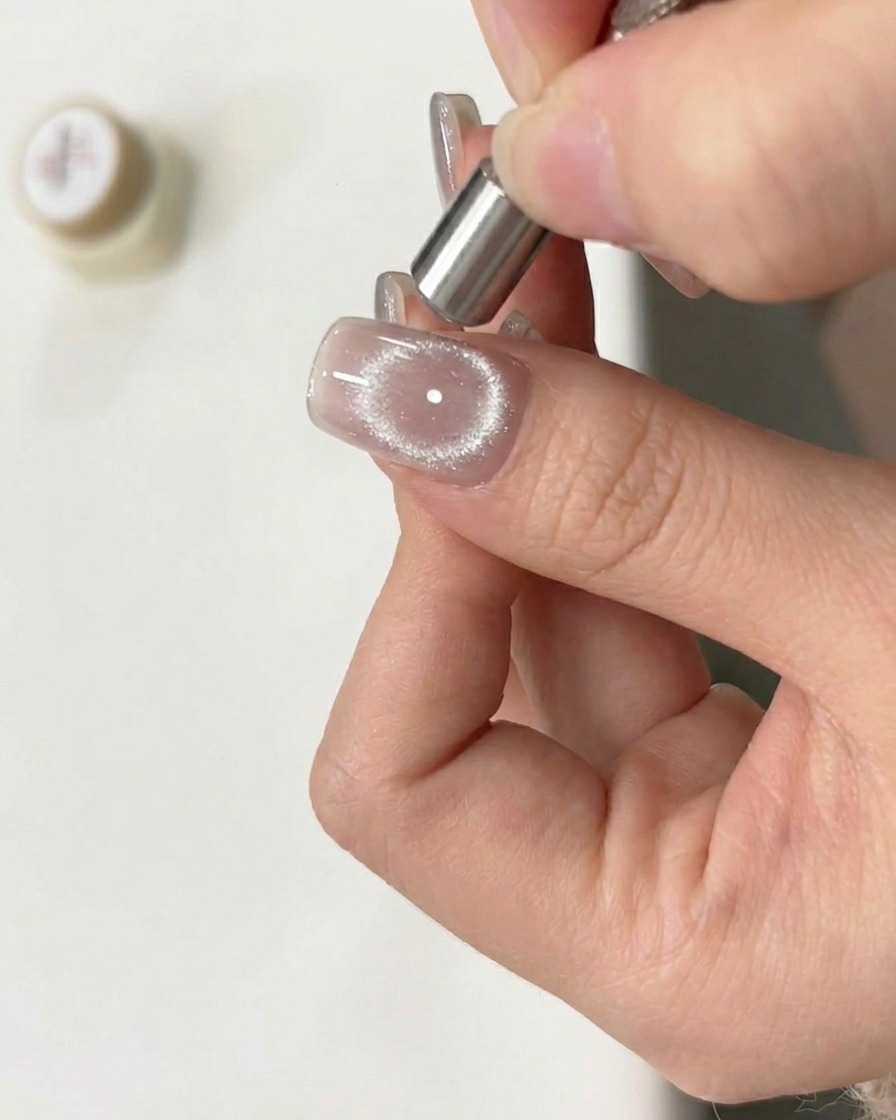 Un magnete tenuto in movimento circolare sopra ununghia con gel cat eye bagnato per creare un effetto ad anello.