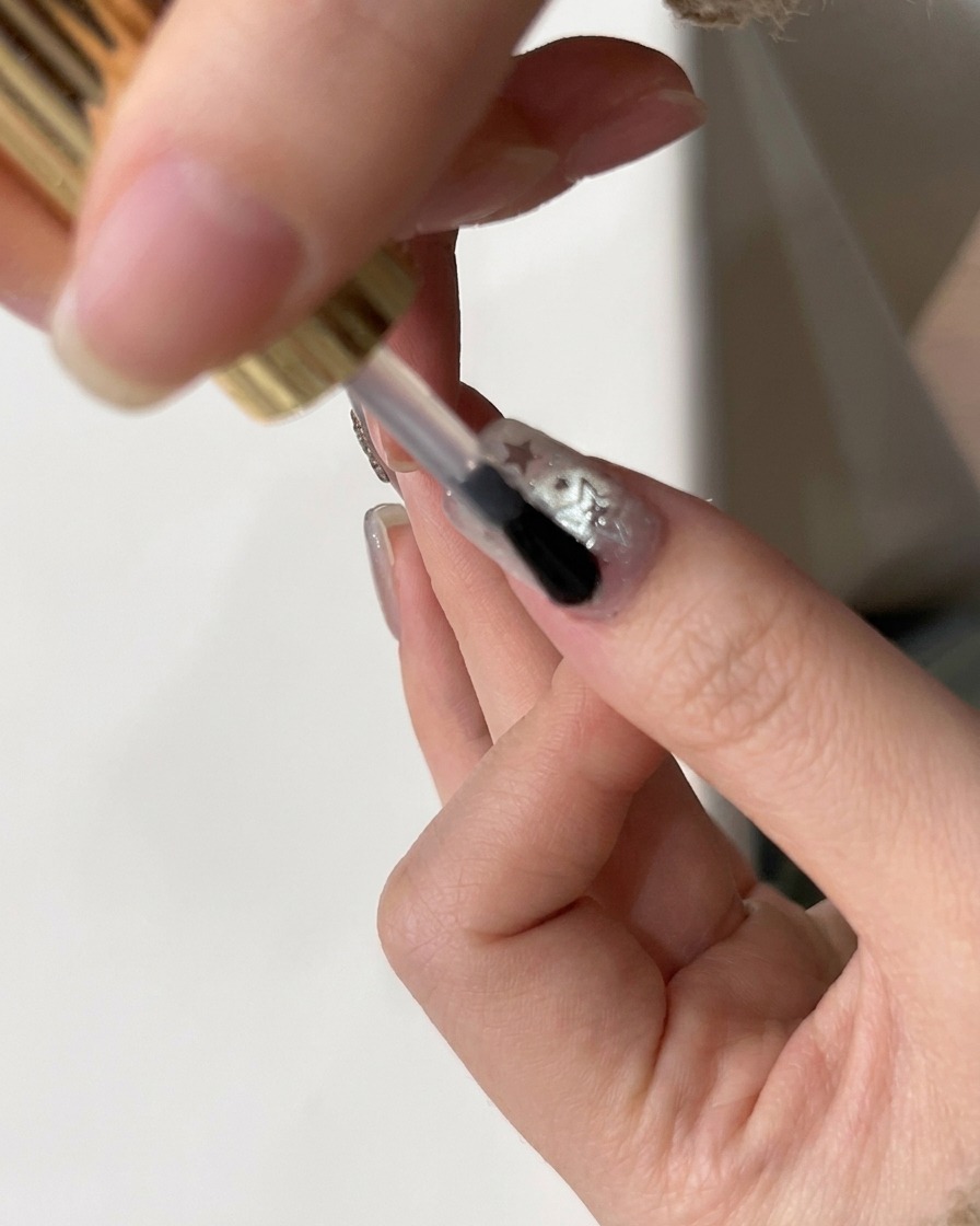 Un pennello applica un top coat lucido finale su ununghia decorata con glitter a stella.