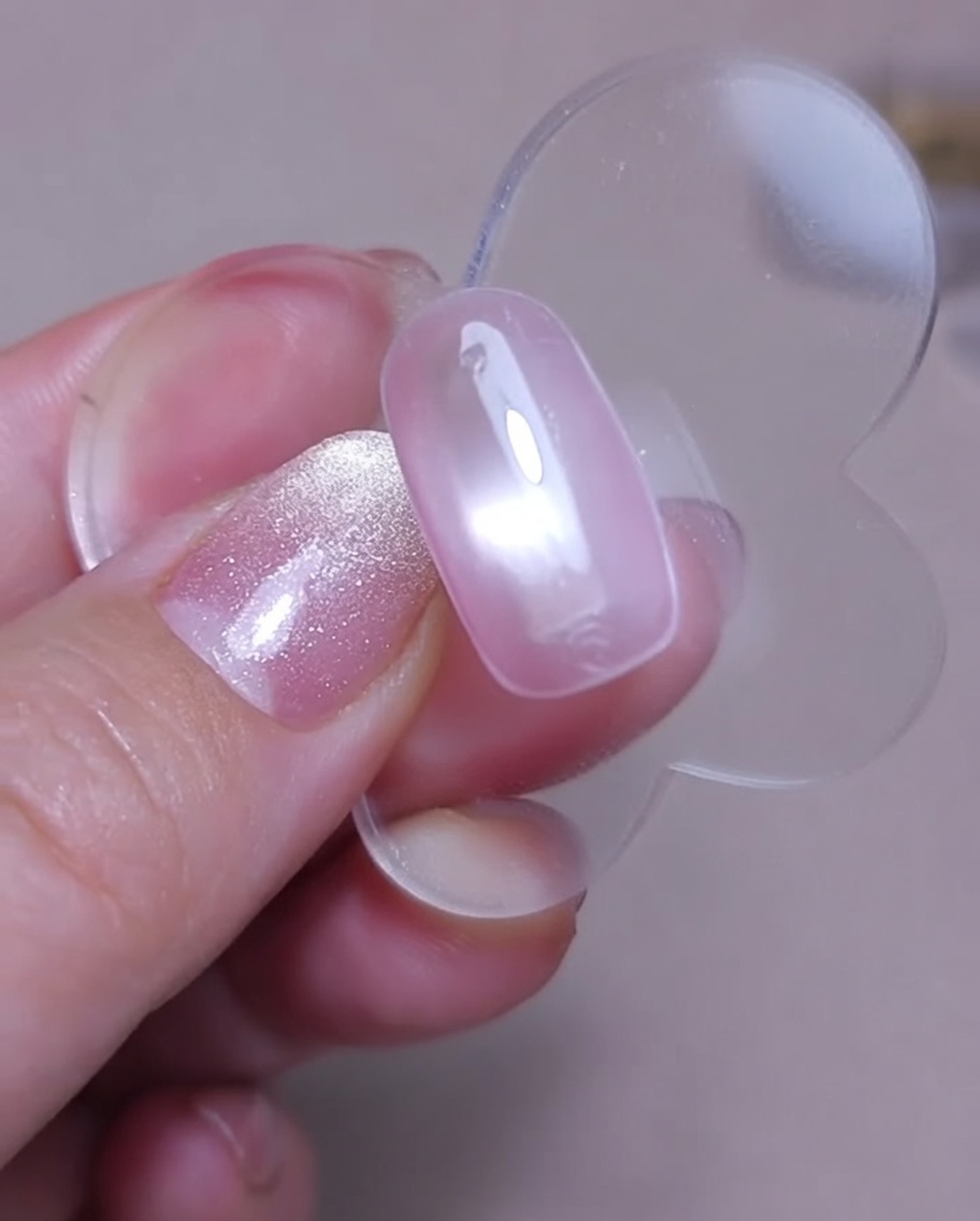 Vista ravvicinata di un magnete tenuto sopra ununghia con gel cat-eye ancora umido per creare un effetto brillante.