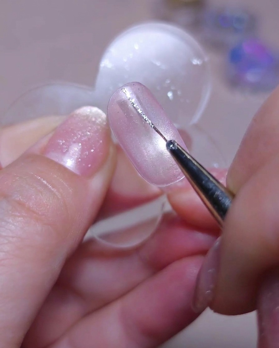 Un pennello di precisione disegna una delicata linea verticale con gel glitter argento sul lato sinistro di ununghia cat-eye.