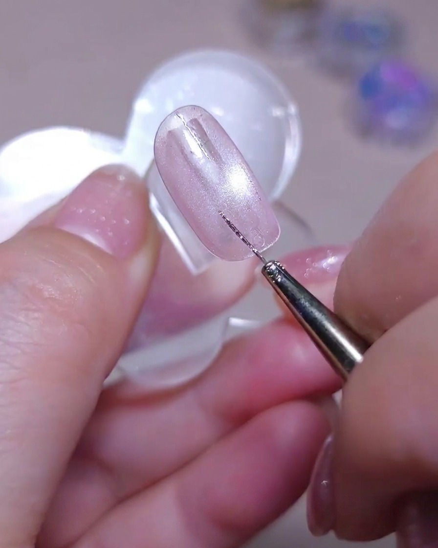 Un pennello sottile disegna una seconda linea verticale dritta di glitter argento accanto a una linea esistente su ununghia cat-eye rosa brillante.