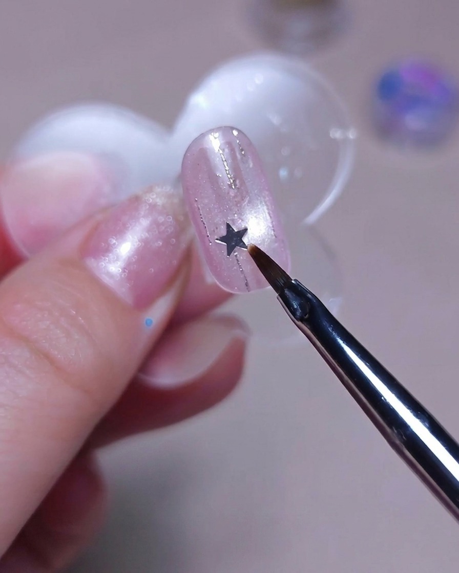 Un pennello sottile posiziona una piccola stellina argento su ununghia.
