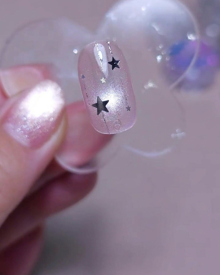 Un pennello applica uno strato finale di top coat trasparente lucido sopra ununghia decorata con linee verticali e stelline argento.
