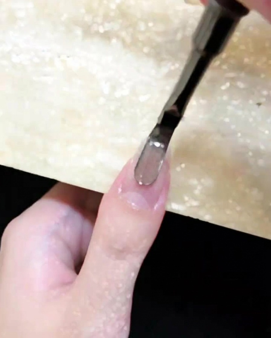 Primo piano di un pennellino che applica il gel cat-eye marrone su ununghia naturale.