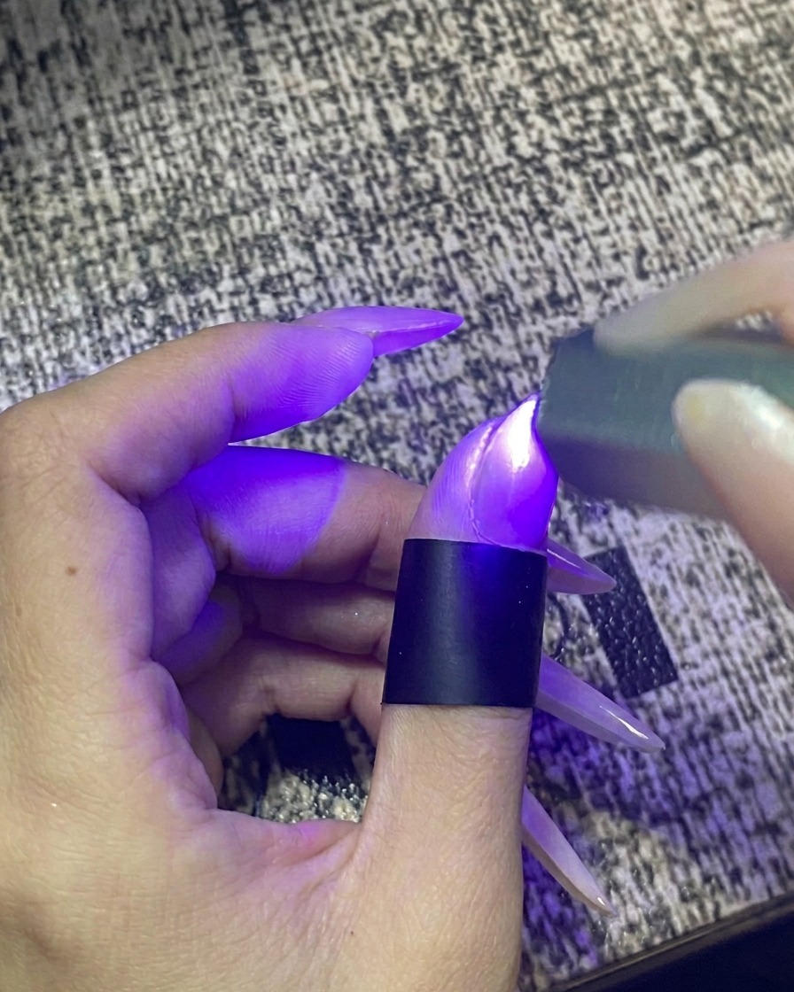 Un dito inserito allinterno di una lampada per unghie UV/LED portatile accesa.