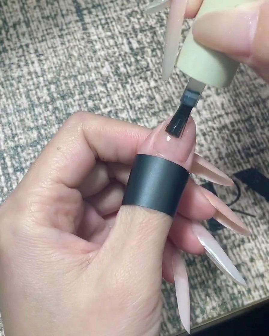 Un pennellino che applica con precisione il top coat trasparente solo sulla metà superiore di ununghia laccata di color nude.