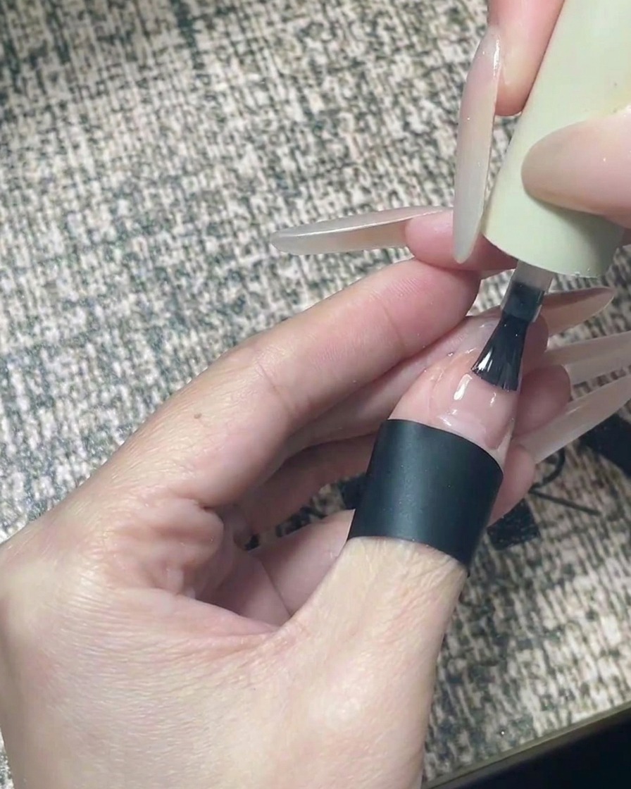 Un pennello che applica un lucido top coat trasparente su un design per unghie finito con stelle nere.