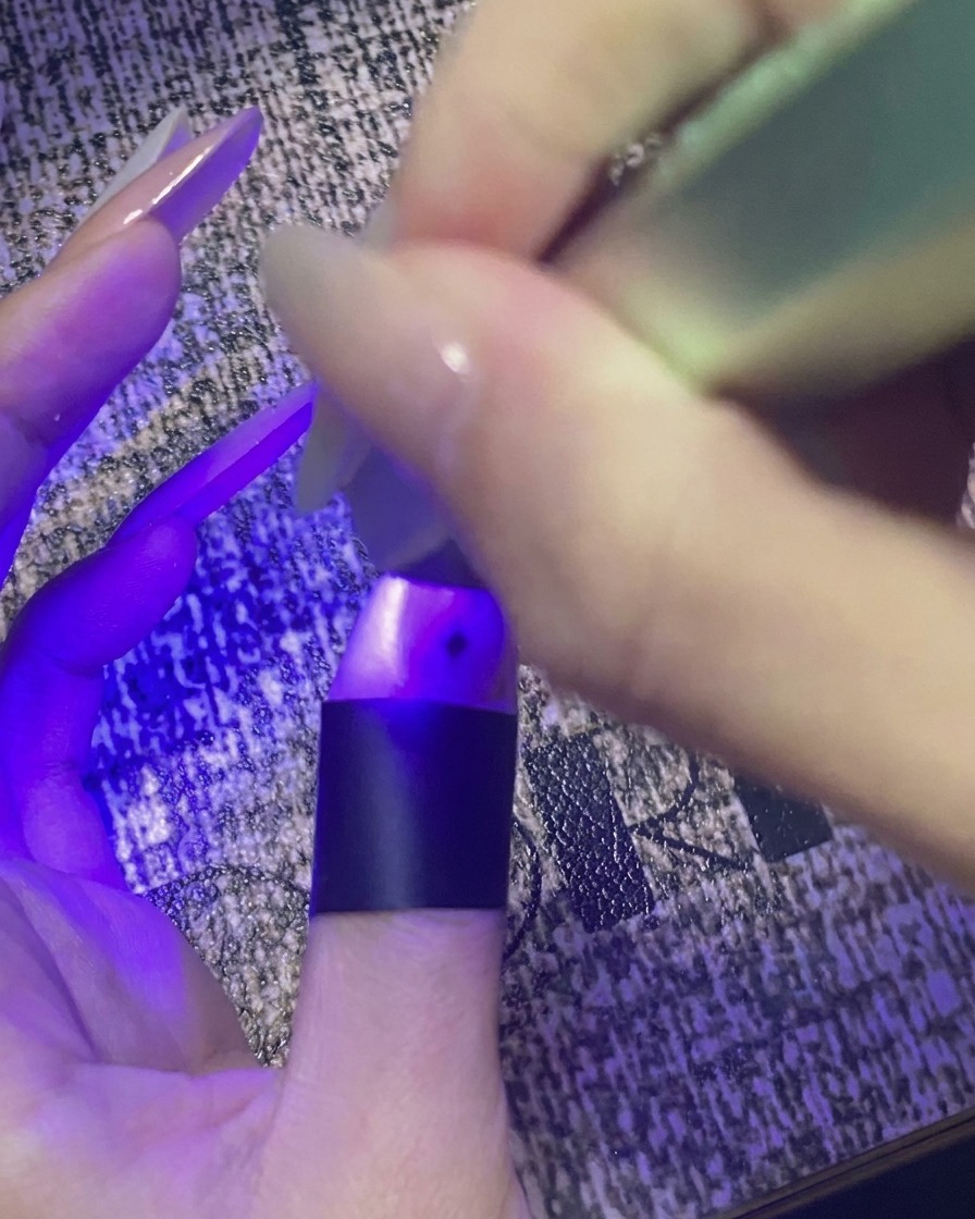 Un pollice con nail art a stella che polimerizza sotto una mini lampada UV/LED viola.
