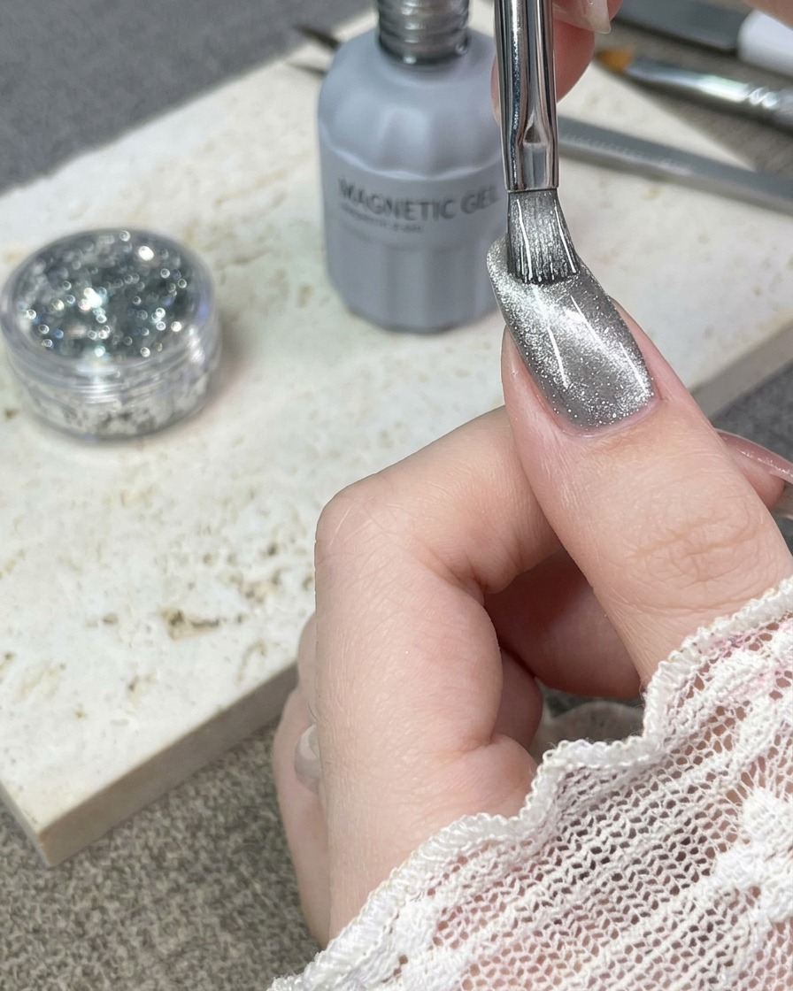Un pennello che applica uno strato di smalto gel cat-eye argento su ununghia naturale.
