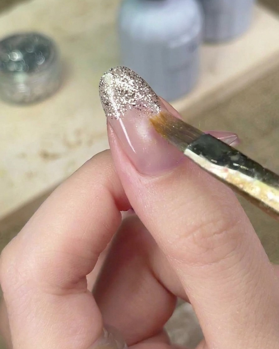 Un pennello sottile che sfuma con cura i bordi del gel glitter sullunghia per perfezionare il gradient.